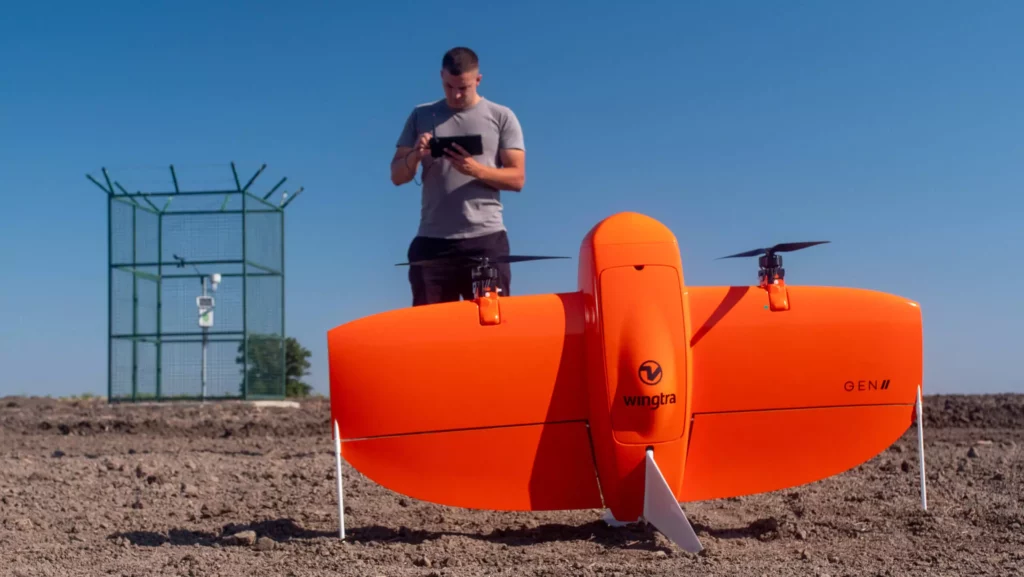 Wingtra drone operated by a man standing behind it on the field, covered with soil.