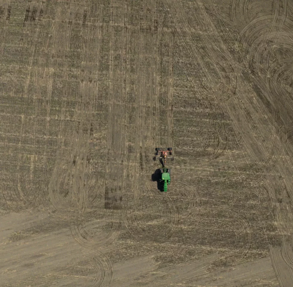 John Deer tractor on the big field covered with soil. Photo taken by drone from the air from high altitude.