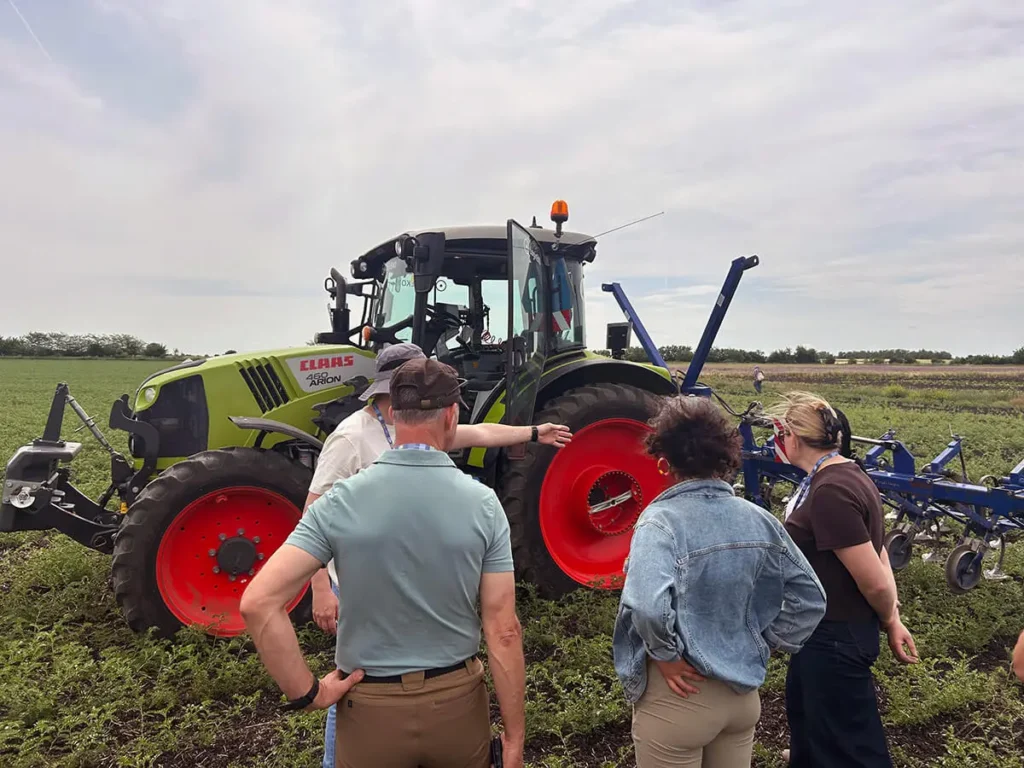 Participants gathered around a Claas Arion tractor with an inter-row cultivator in a chickpea field at LoginEKO