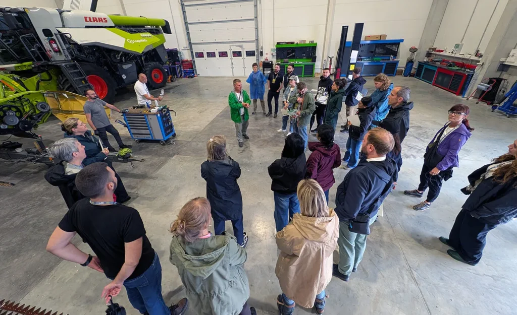 Group gathered for a facility tour in the LoginEKO mechanization workshop, with a Claas Lexion combine and header in the bay