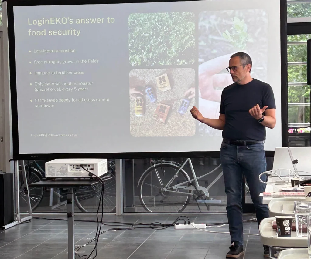 Speaker presenting a slide titled LoginEKO's answer to food security, listing low-input production and farm-saved seeds, at the Lighthouse Farm Lab