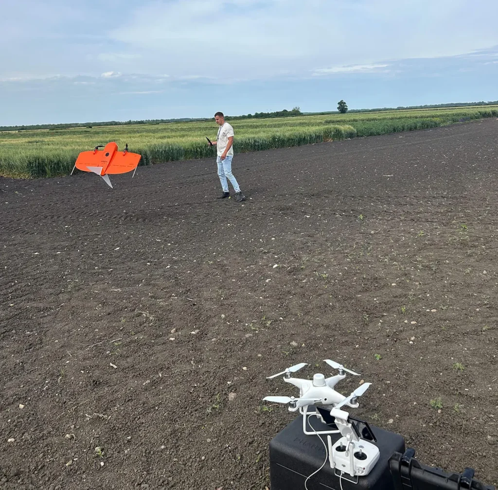 Wingtra fixed-wing drone on a field edge beside oat variety trial plots at LoginEKO, with a DJI Phantom drone and controller in the foreground