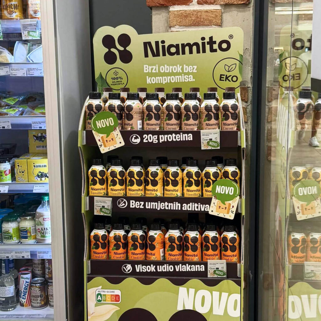 Niamito branded floor display in a store with Cocoa, Vanilla and Cookie bottles on three shelves, Croatian signage reading 20g proteina, bez umjetnih aditiva, visok udio vlakana